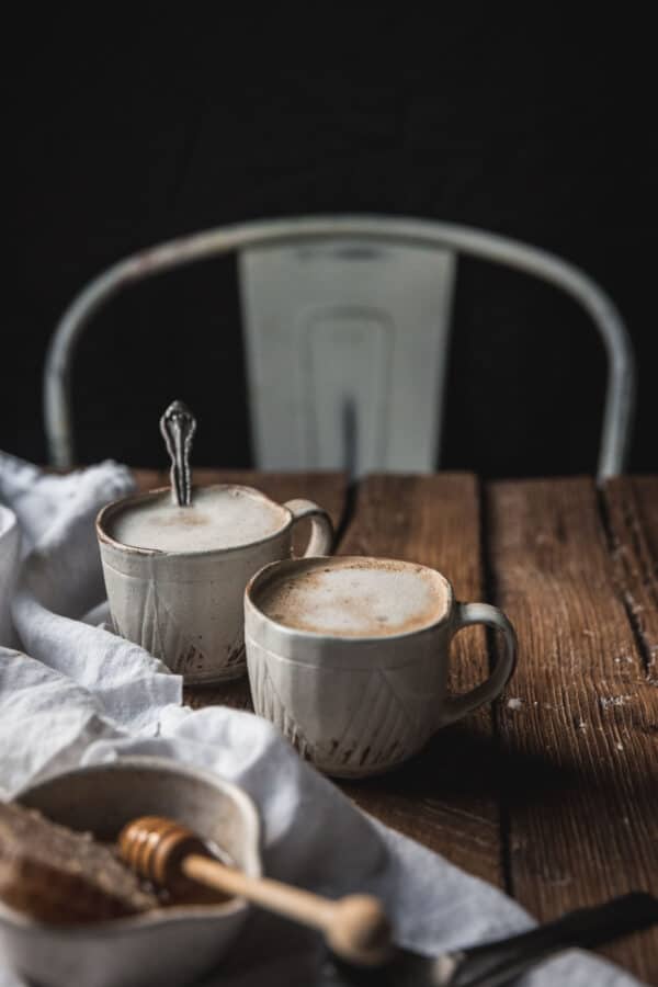 two lattes on a distressed wood table with napkins and honey