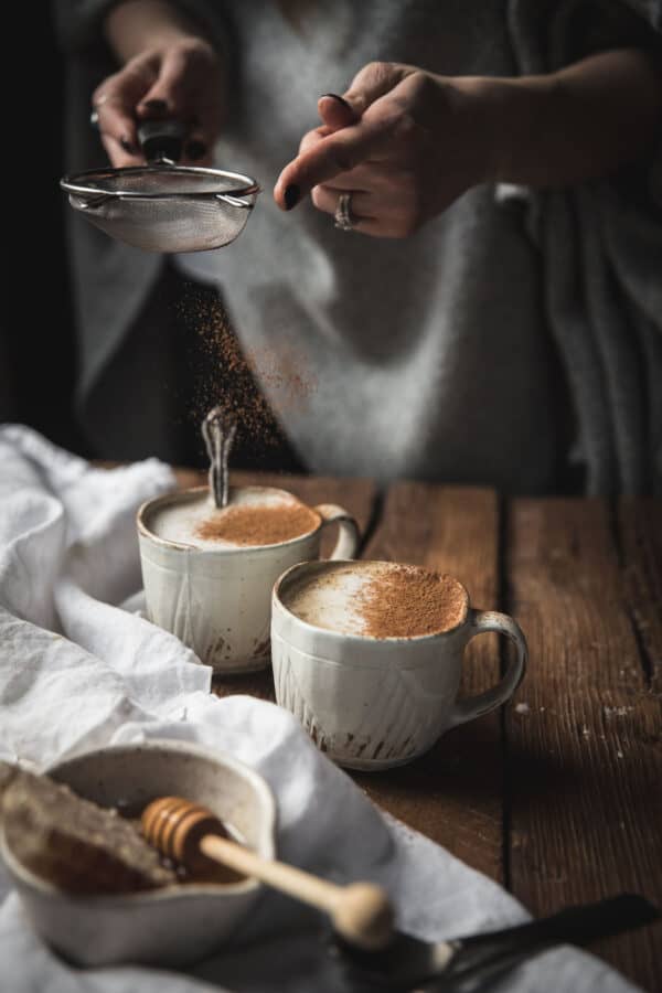 dusting cinnamon over oat milk lattes