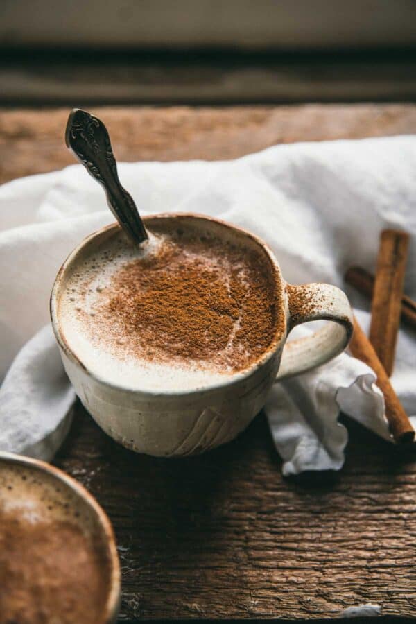 close up of cinnamon dusting foam on top of a latte in a white ceramic mug