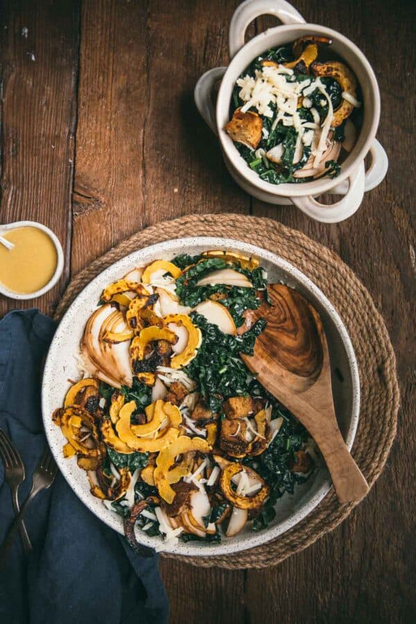 overhead of kale salad in a serving bowl with dressing and side dish of salad