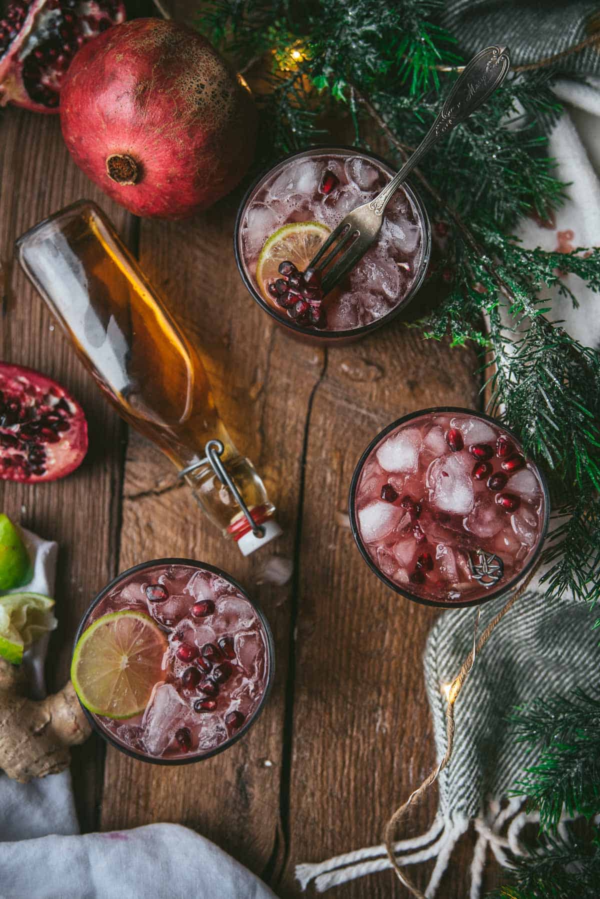 overhead of three pomegranate cocktails and bottle of bourbon on would background