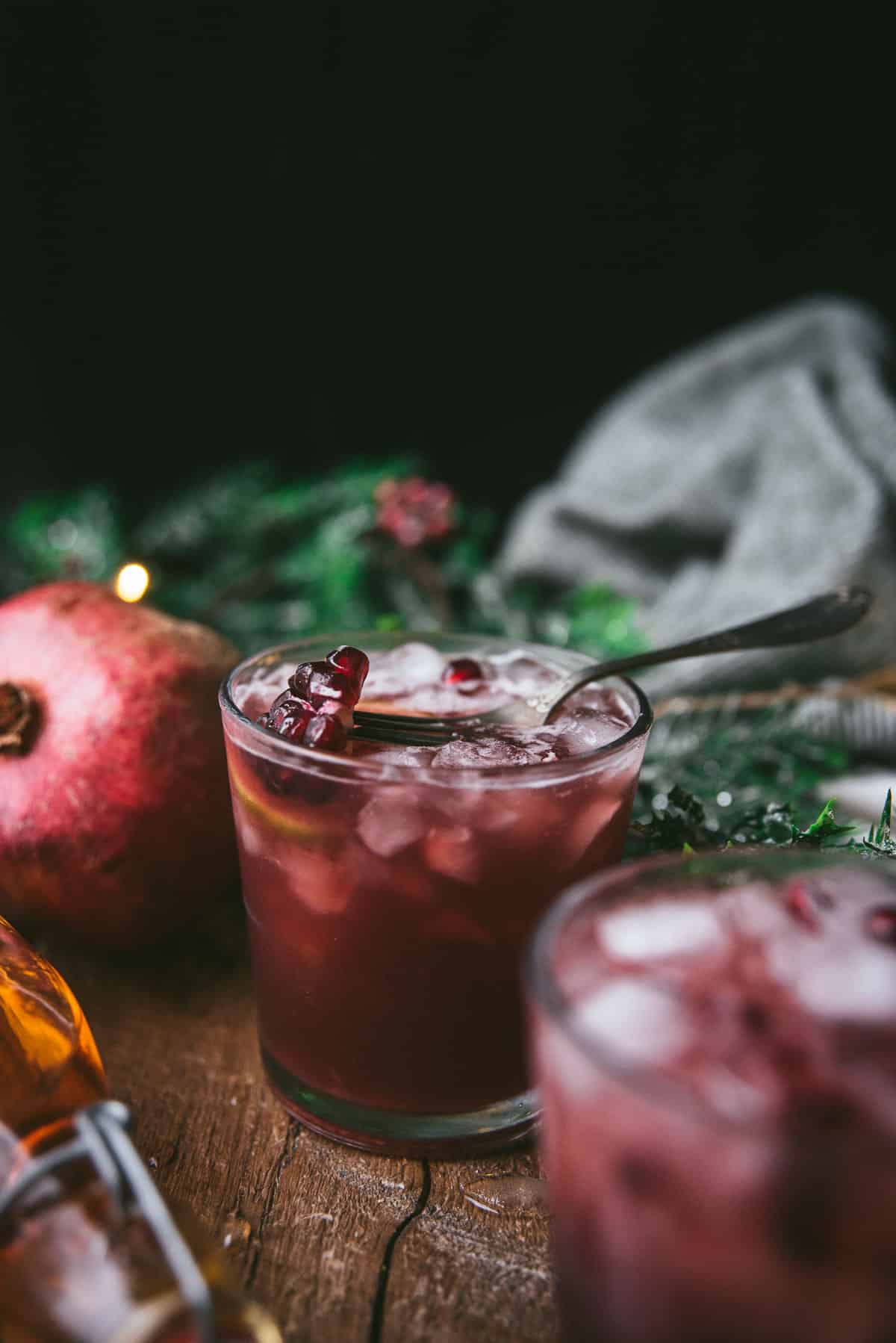 high ball glass with dark pomegranate bourbon cocktail and pomegranate seeds