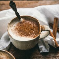 close up of cinnamon dusting foam on top of a latte in a white ceramic mug