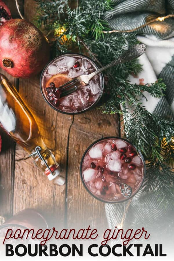 overhead of two pomegranate cocktails and bottle of bourbon on wood background