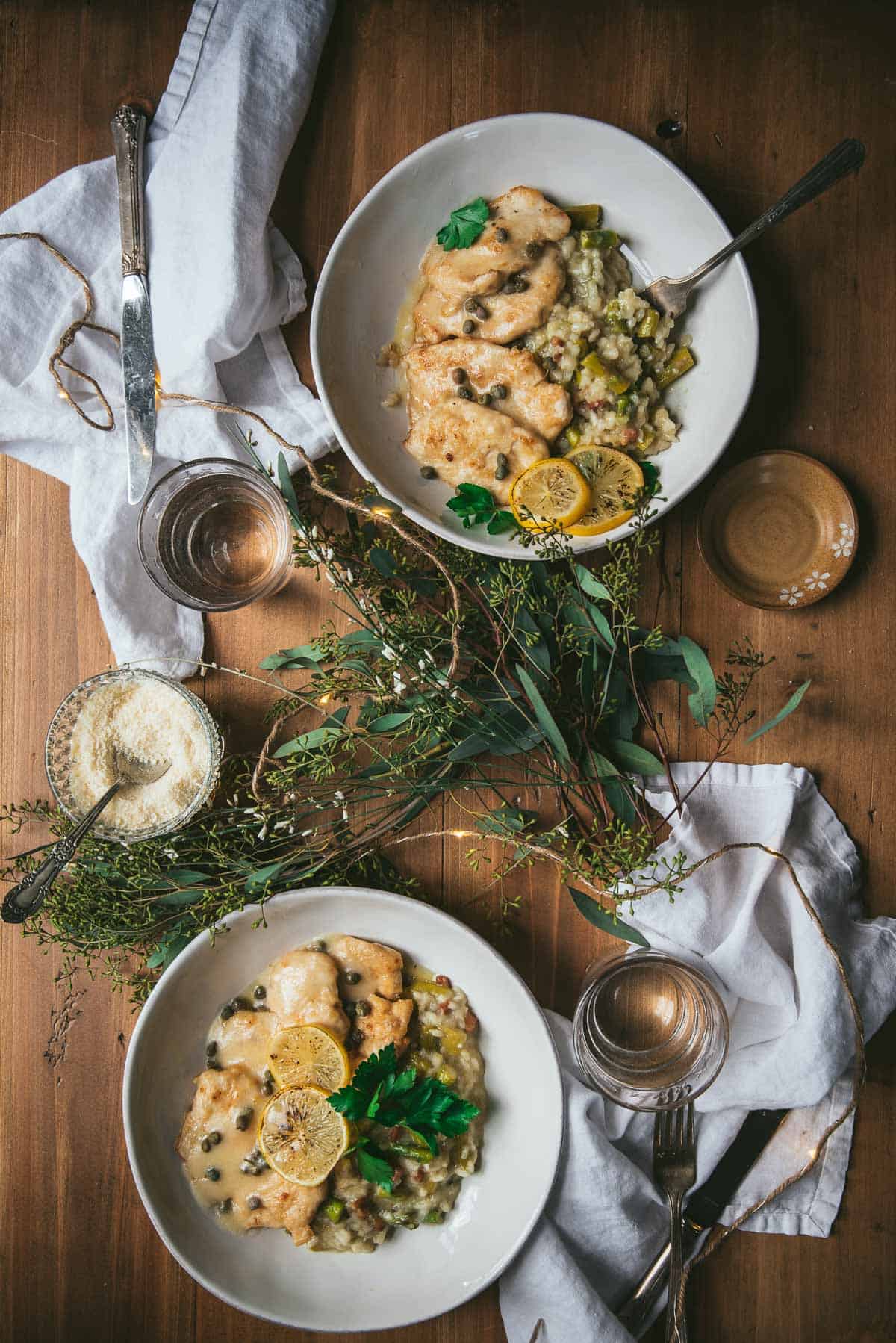 two servings of chicken piccata and risotto on plates with flowers and lights