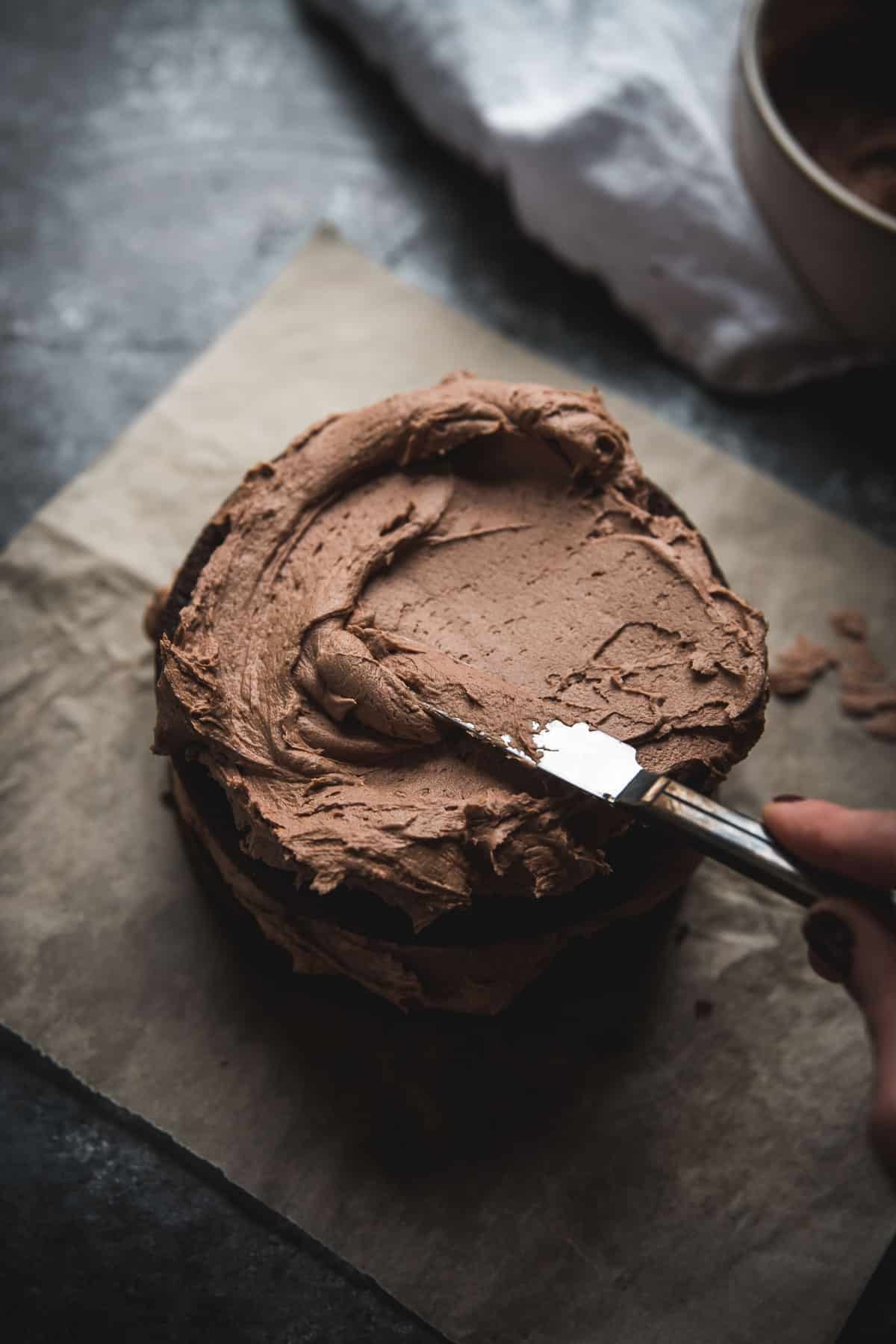spreading chocolate buttercream on a small layer cake