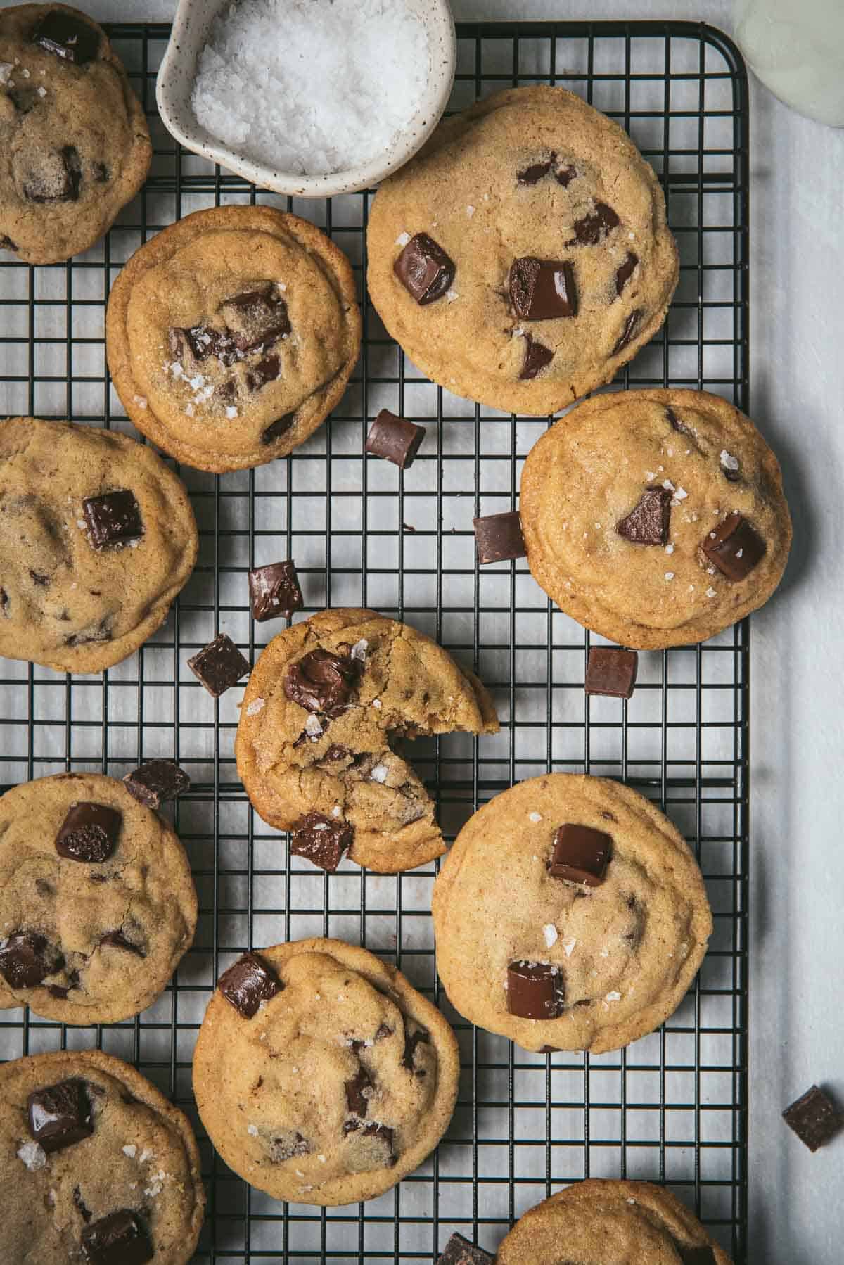 overhead of chocolate chip cookies on a baking rack with sea salt flakes in a bowl