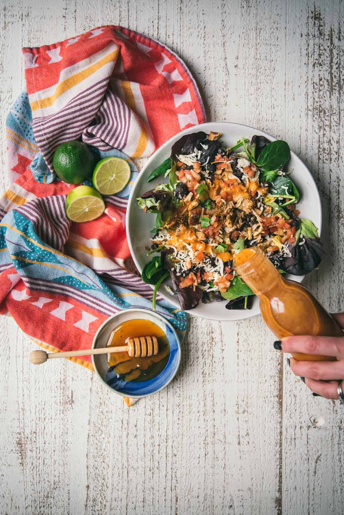 drizzling salad dressing over a loaded salad