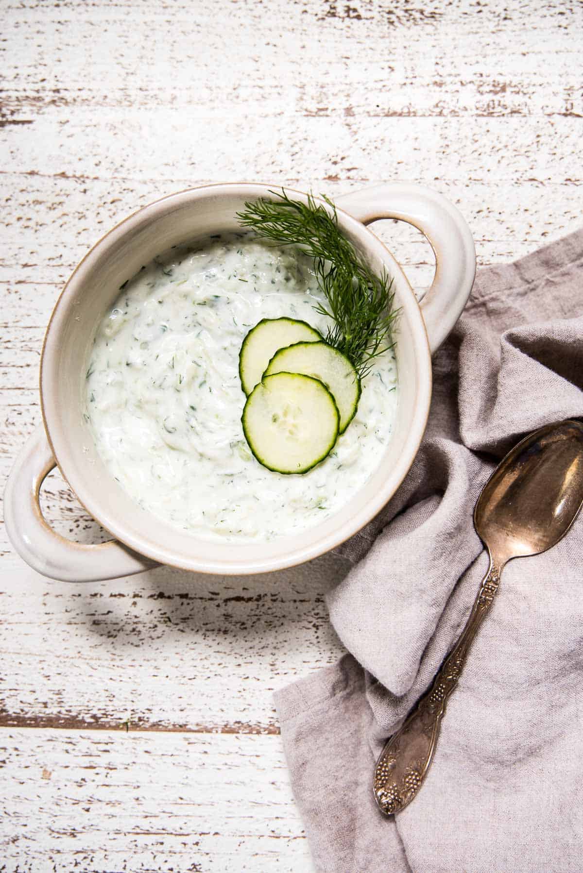 overhead shot of tzatziki sauce in a bowl topped with cucumber slices and fresh dill sprig