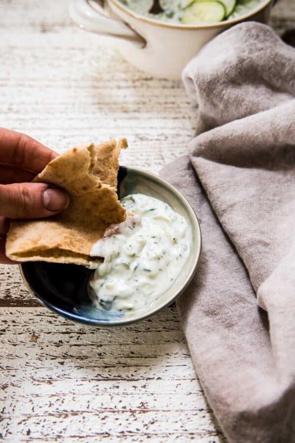 pita scooping greek cucumber yogurt sauce out of a side plate