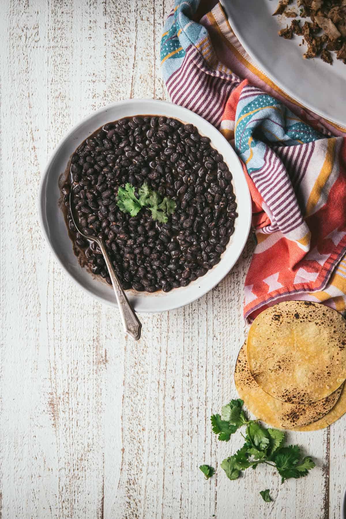 overhead of black beans in a bowl with colorful napkins and tortillas