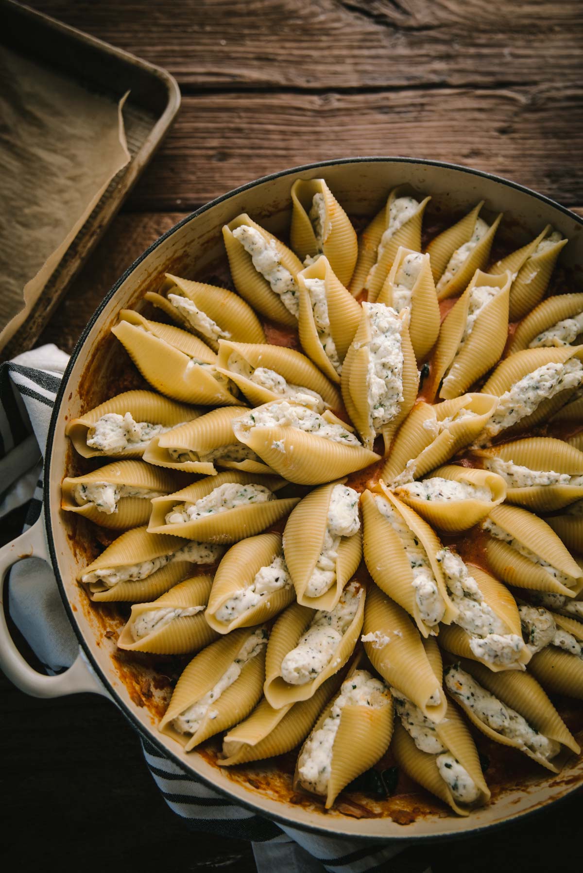 Unbaked stuffed shells arranged in a circle pattern in a cream colored oven pan over pasta sauce. They have still to be topped with more sauce and cheese.