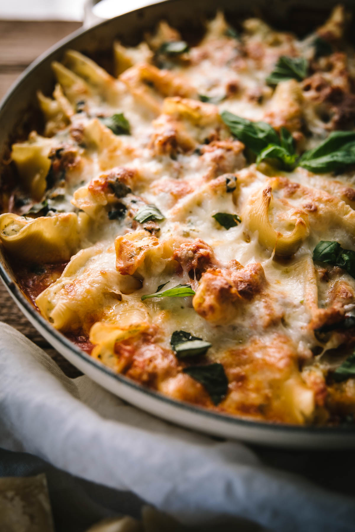 Close up side angle of stuffed shells baked with cheese. You can see all the melted cheese mixed with the sausage meat. Fresh basil is used to garnish.