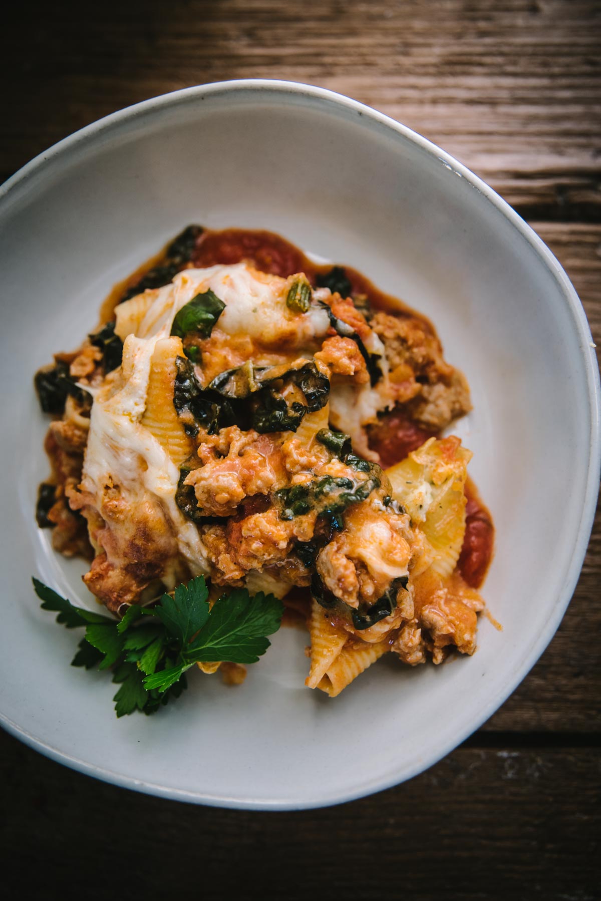 A serving of stuffed shells in a white bowl. There is lots of orange color sauce and meat. It has been garnished with fresh herbs.