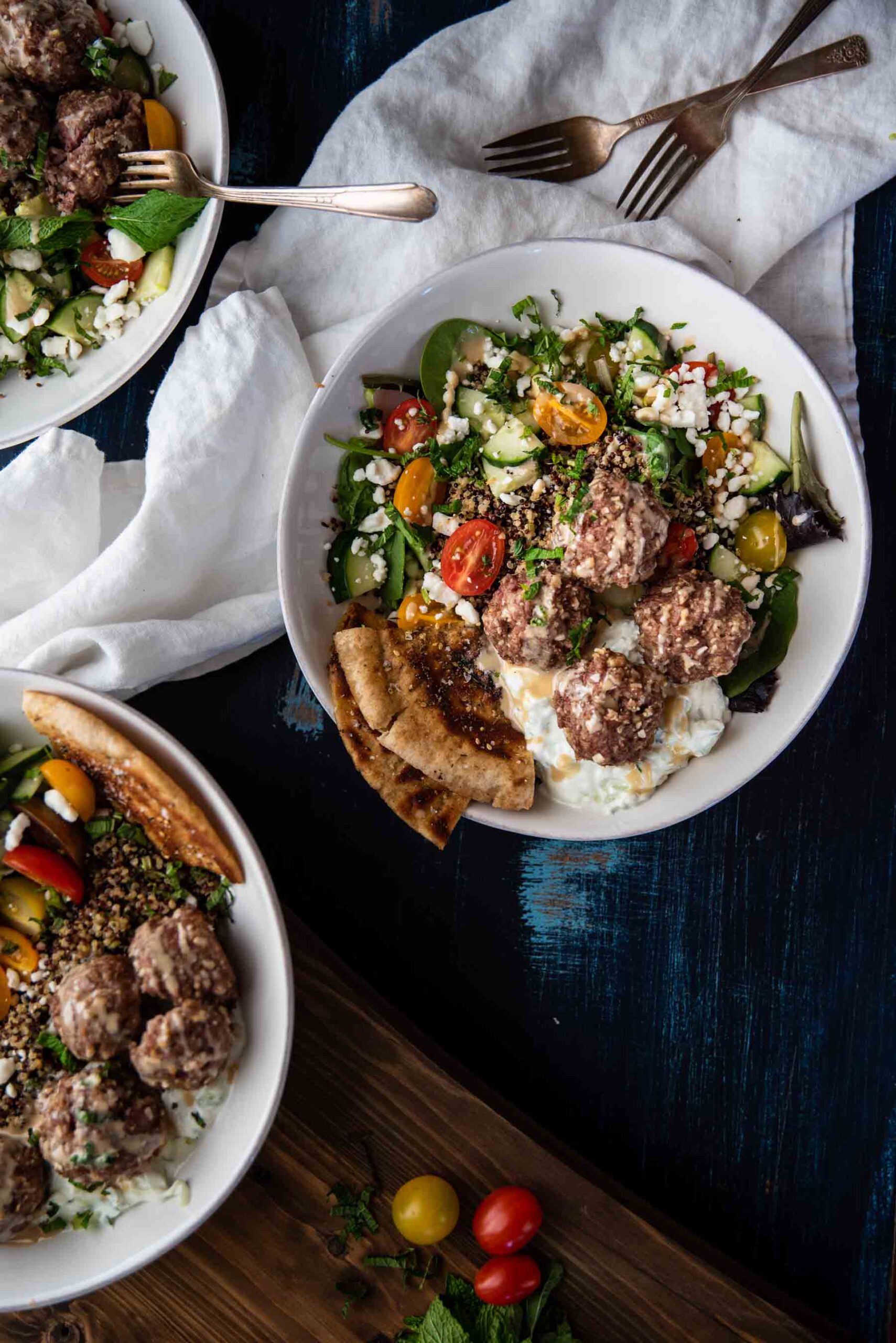 overhead of mediterranean quinoa bowls topped with lamb meatballs and pita