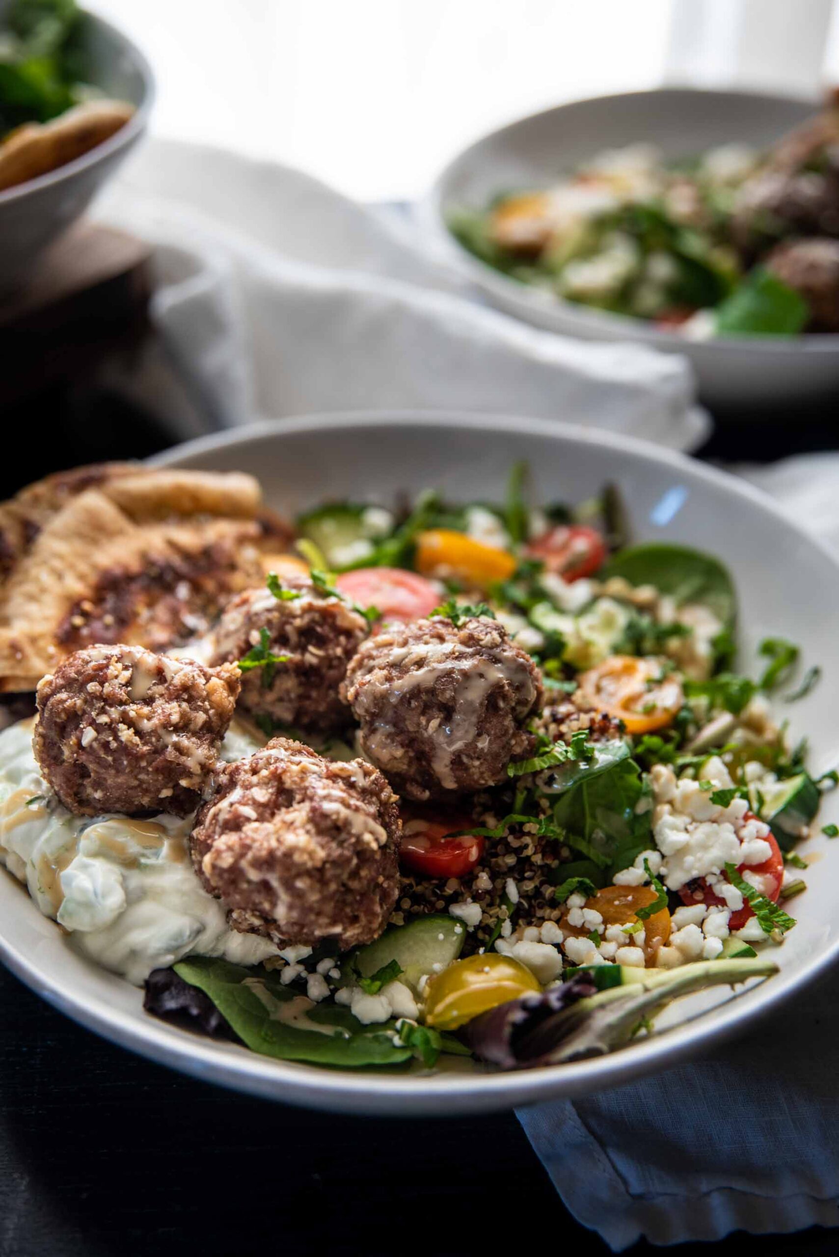 backlit bowl of quinoa, tomatoes, cucumbers, feta, and meatballs