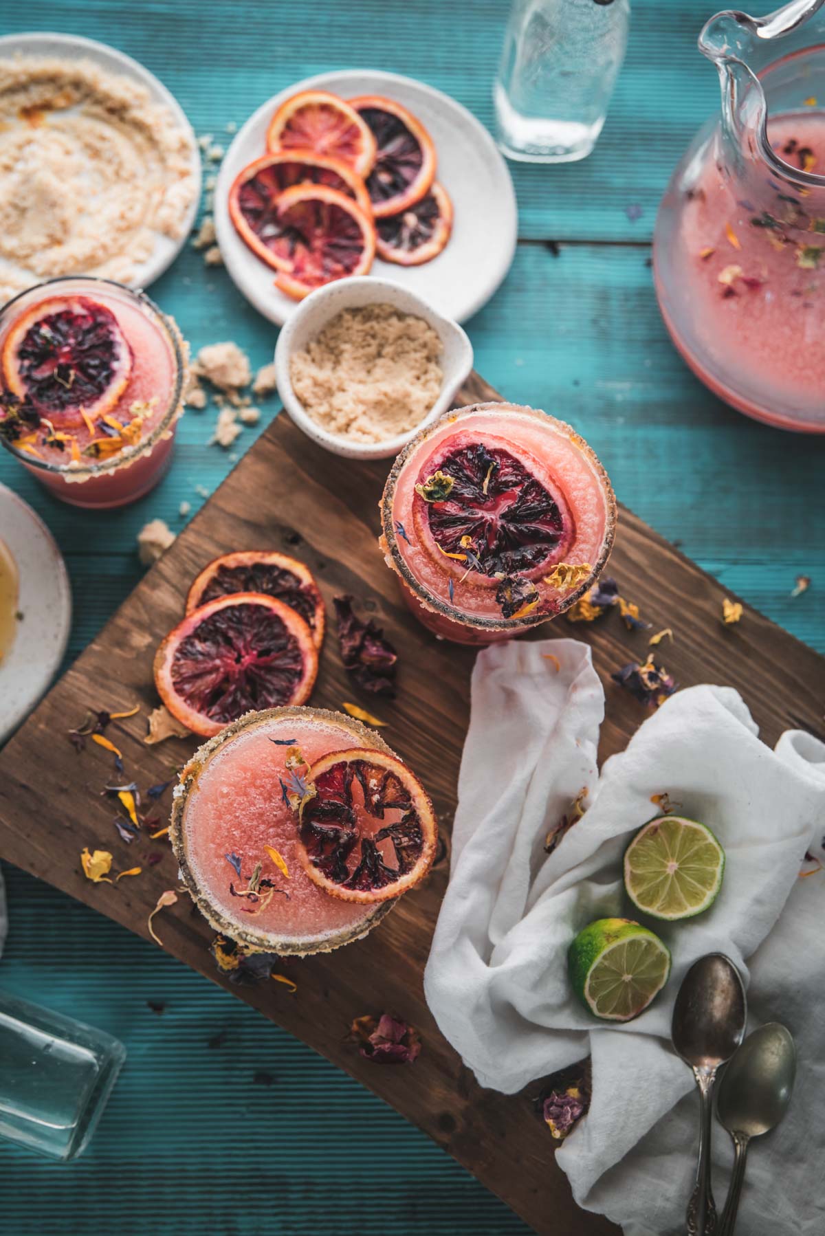 overhead image on frozen blood orange margaritas in glasses with dehydrated orange wheels and edible flowers on top