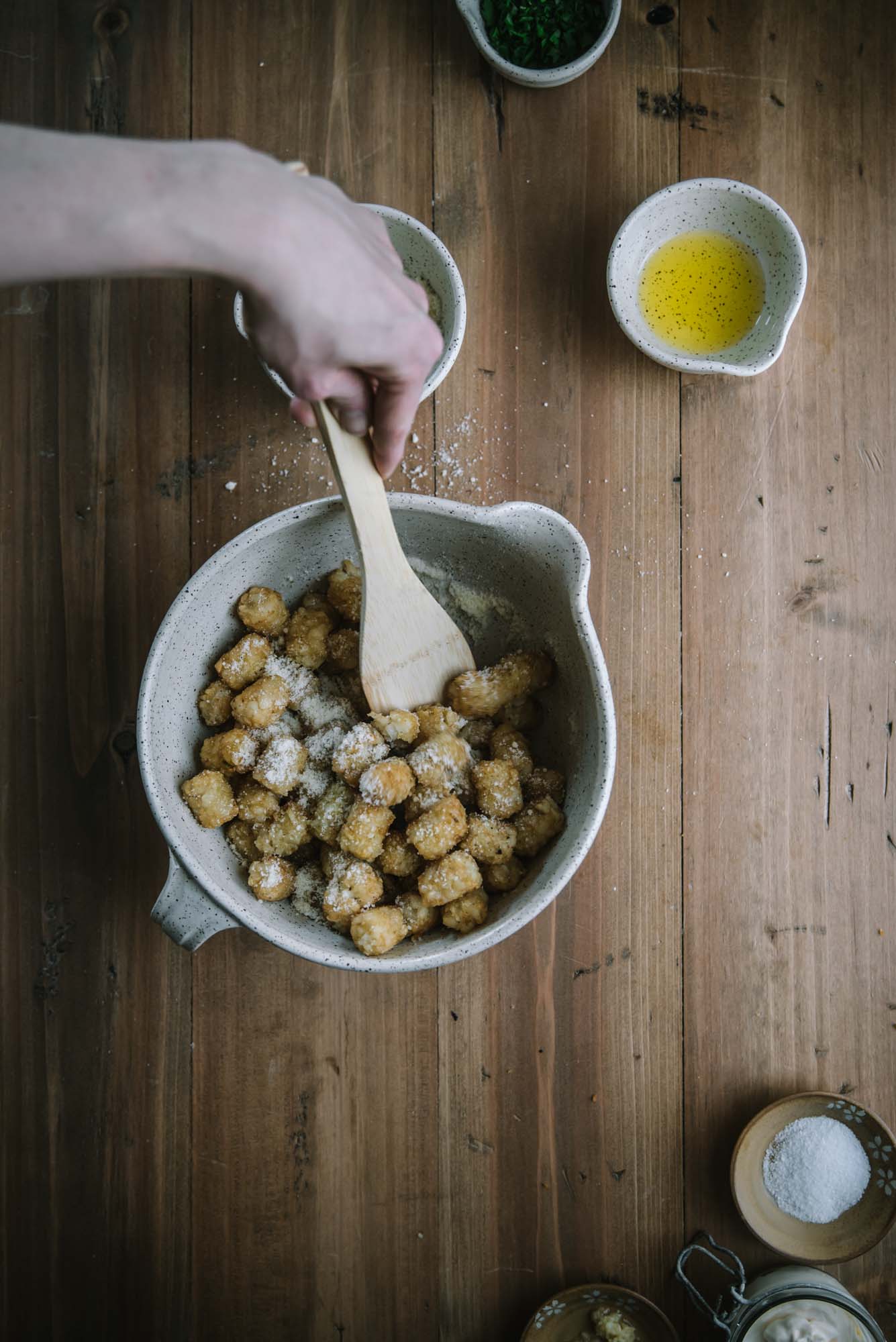 wooden spoon tossing tater tots with parmesan cheese