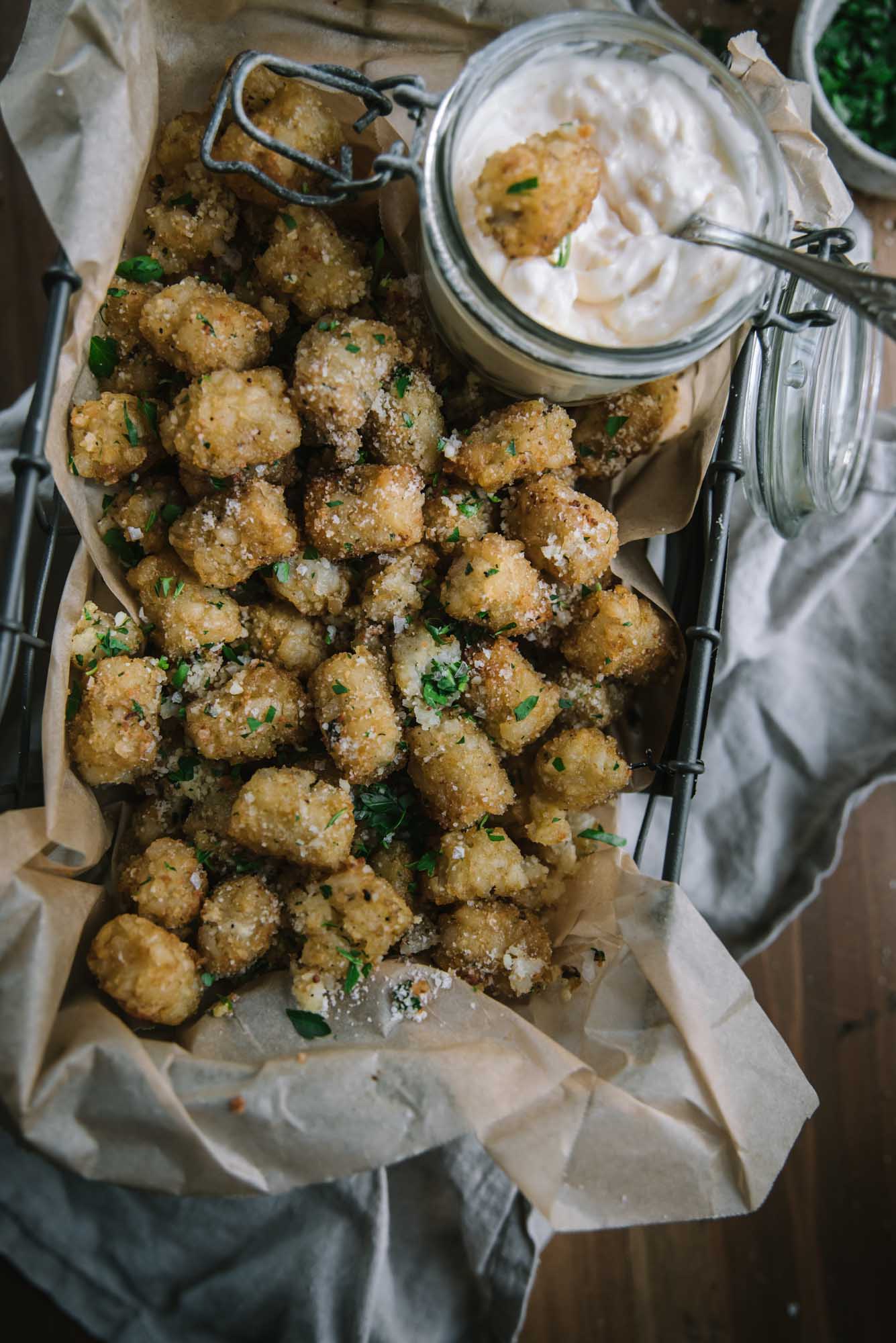 overhead of tater tots in parchment lined basket with garlic aioli