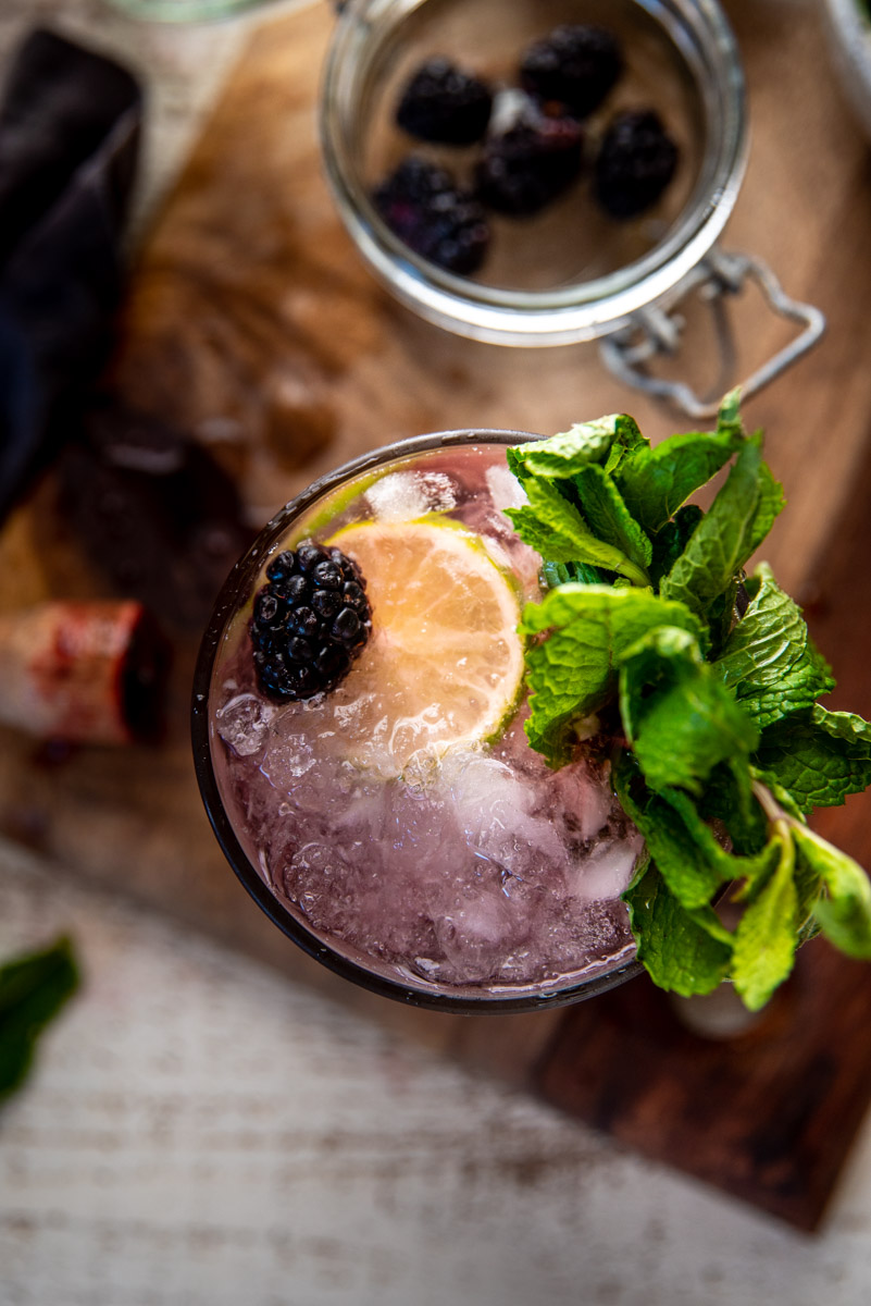 overhead close up of blackberry cocktail in a glass with crushed ice, lime and mint
