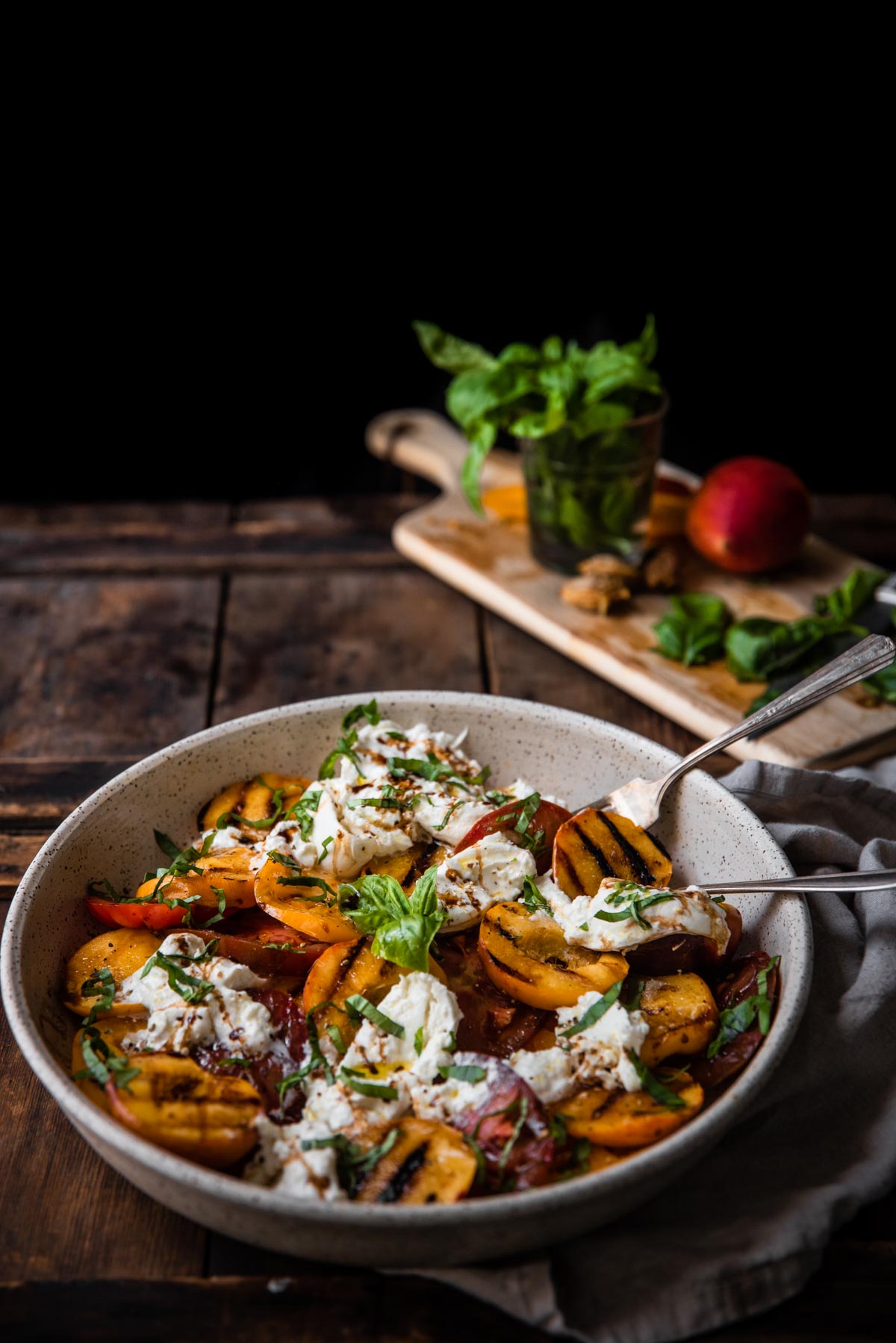 serving spoons in a platter of caprese salad with grilled peaches