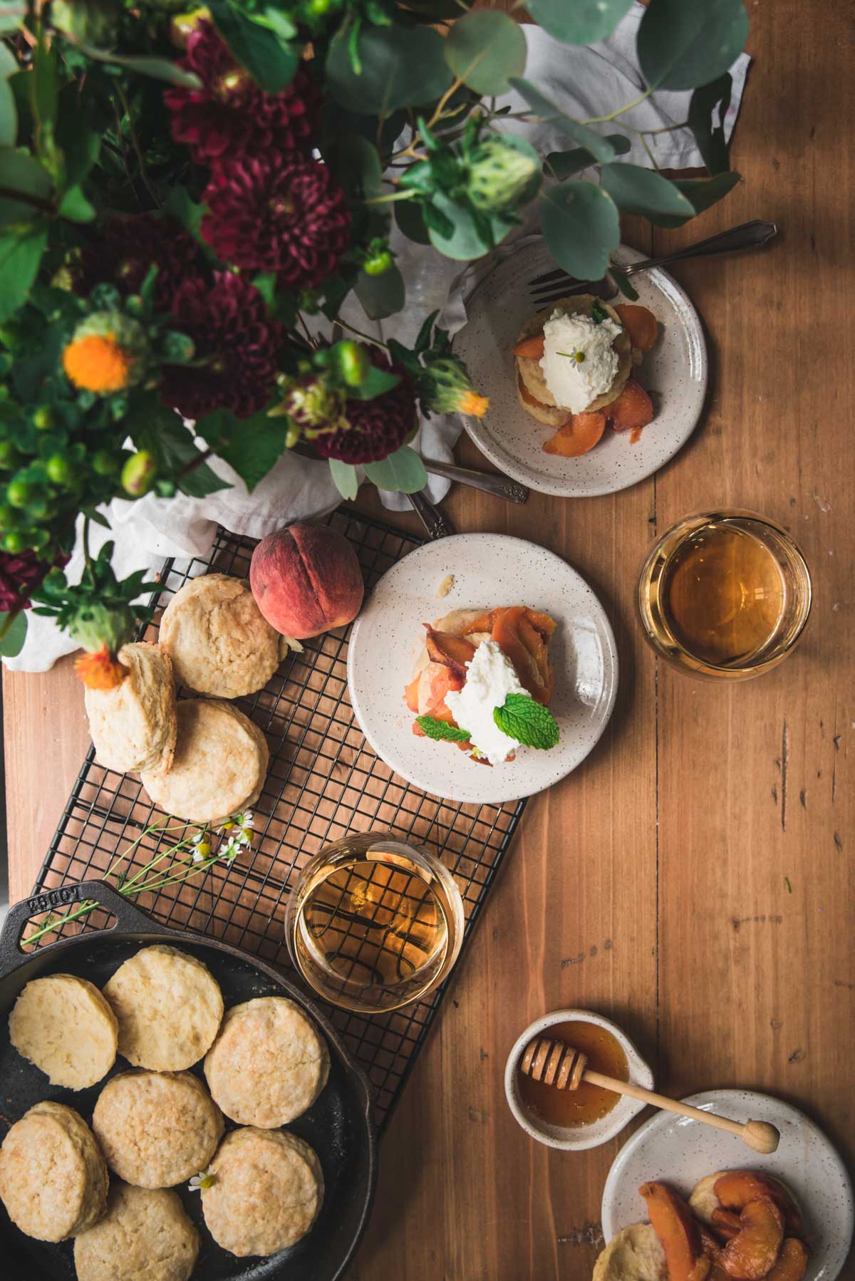 overhead photo of sliced peaches, biscuits, and whiskey glasses