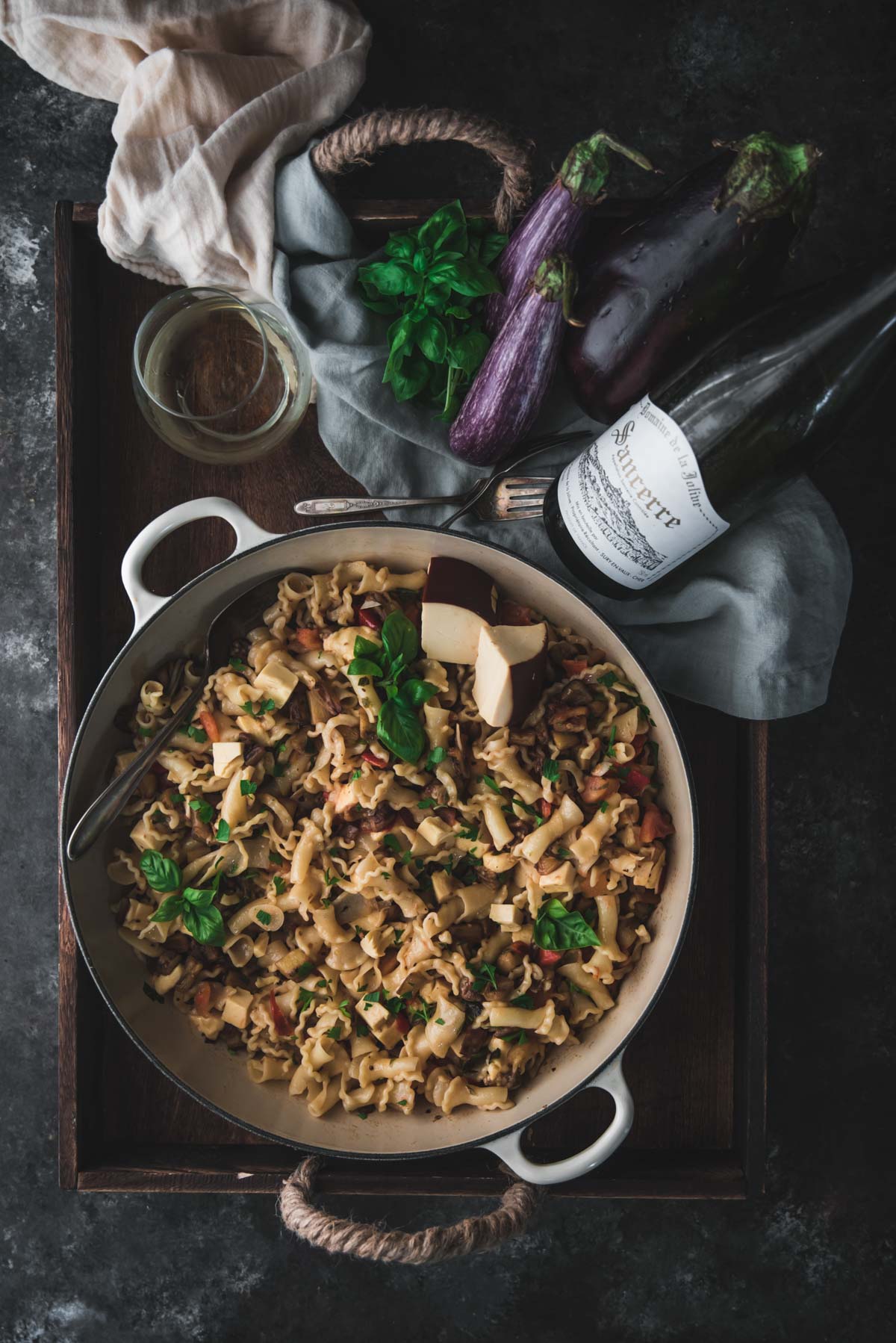 overhead of pasta in a large braiser with eggplants and a bottle wine on a tray