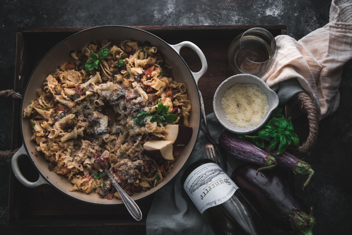 overhead shot of pasta in a braising dish on a tray with wine and cheese