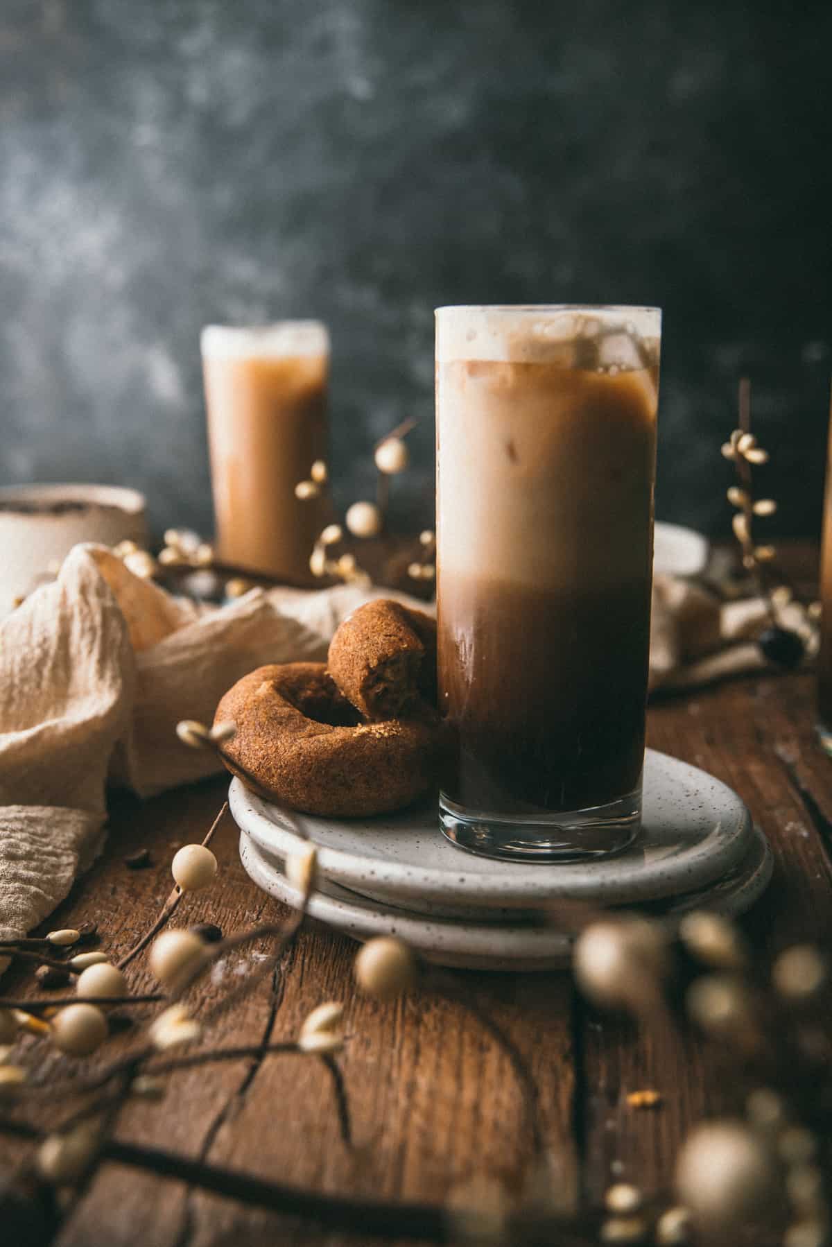 Layers of shaken espresso, ice, and milk in a glass on a plate with cider donuts