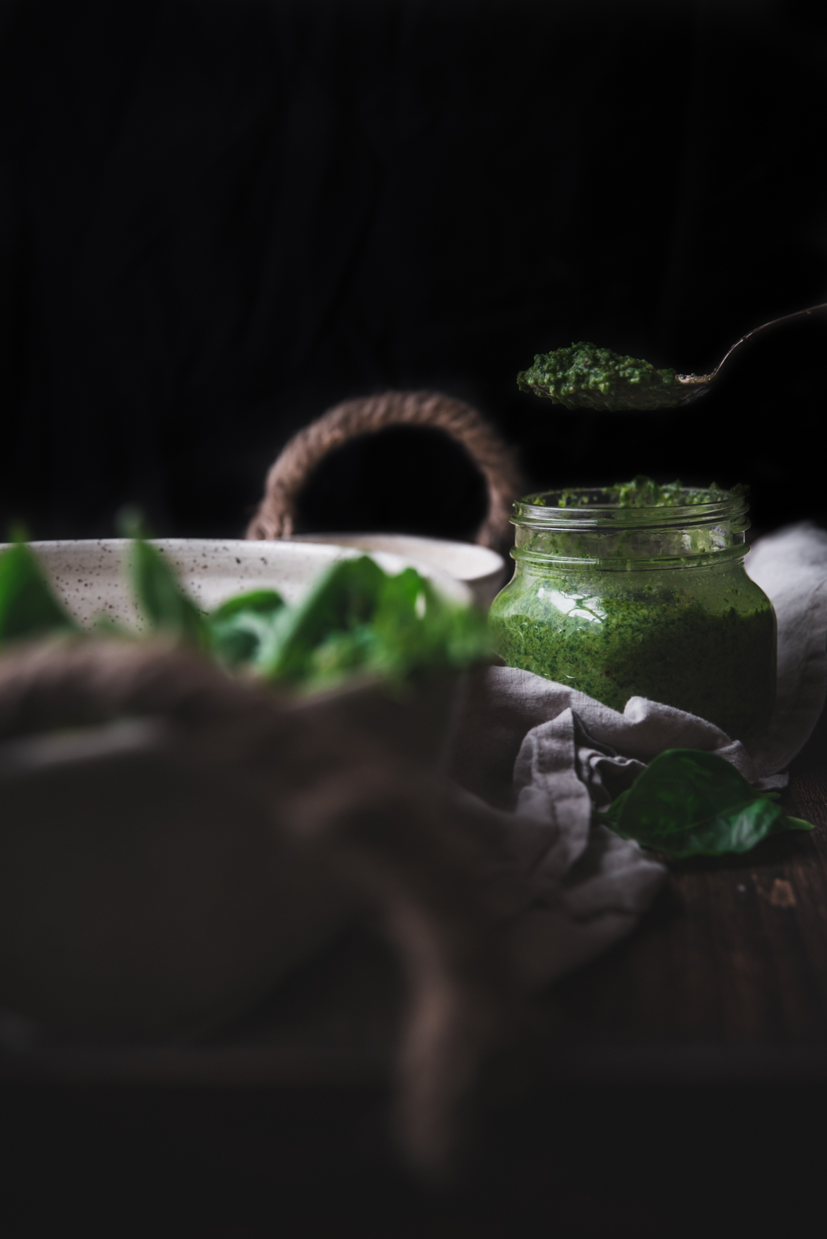 scooping green basil sauce out of a mason jar against a black background