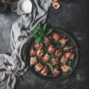 overhead image of prosciutto wrapped figs on a metal tray