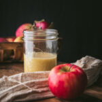 dressing in a mason jar with a red apple in front of the jar