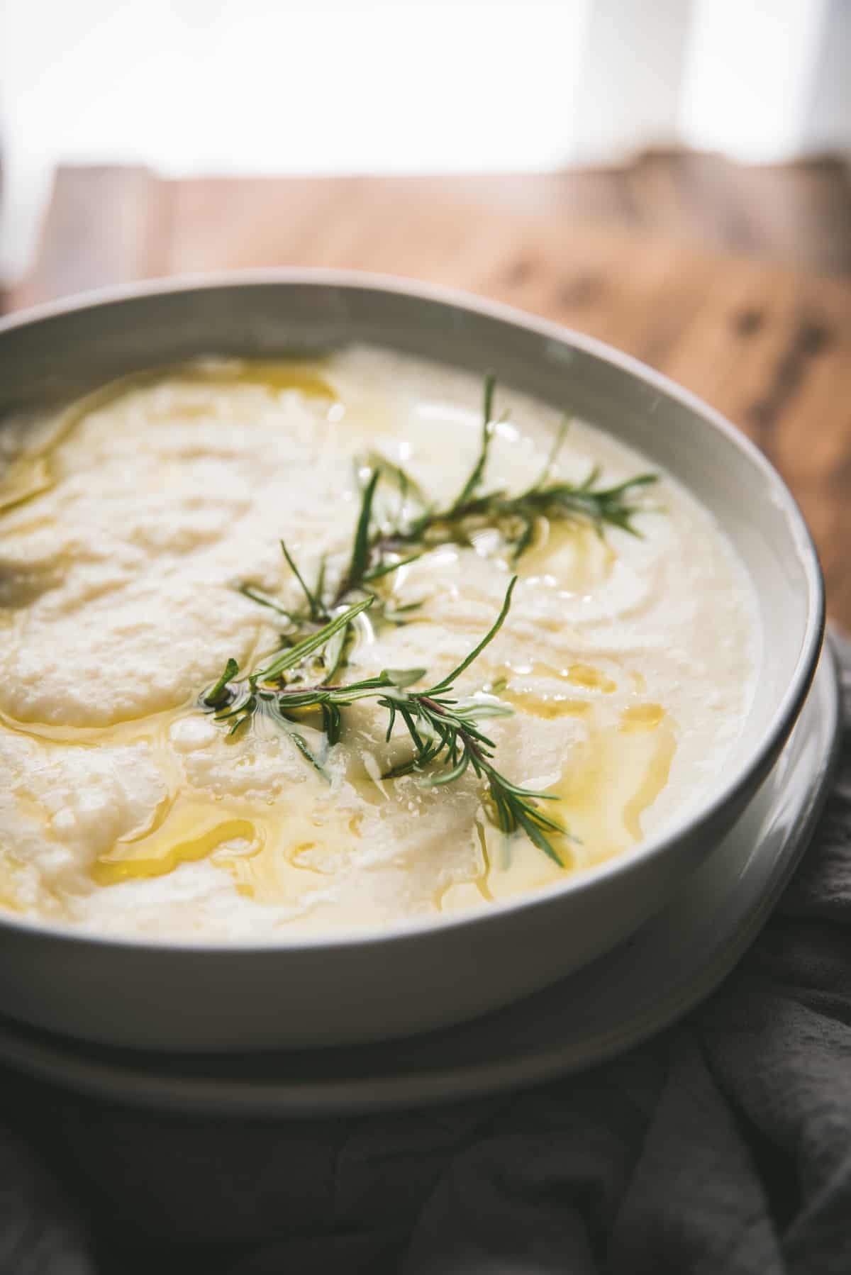 backlit side angle photo of cooked parsnips in a bowl with rosemary sprig on top