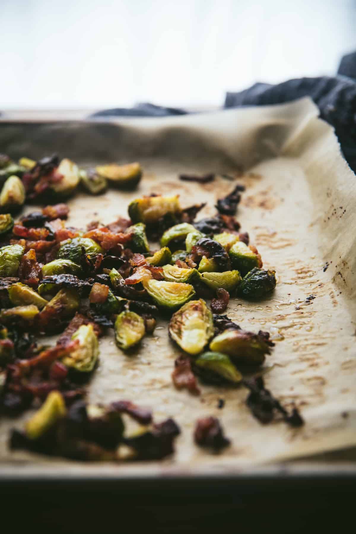 backlit photo of roasted maple brussels sprouts and bacon on a sheet tray with parchment paper