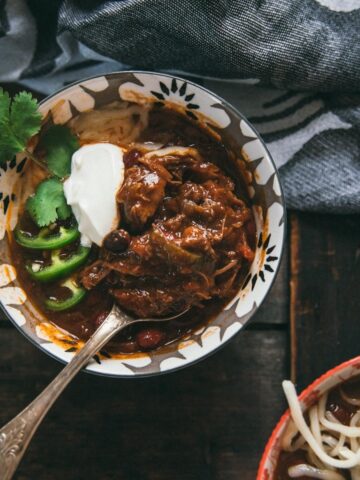 overhead of short rib chili in a bowl with sour cream and jalapeño slices