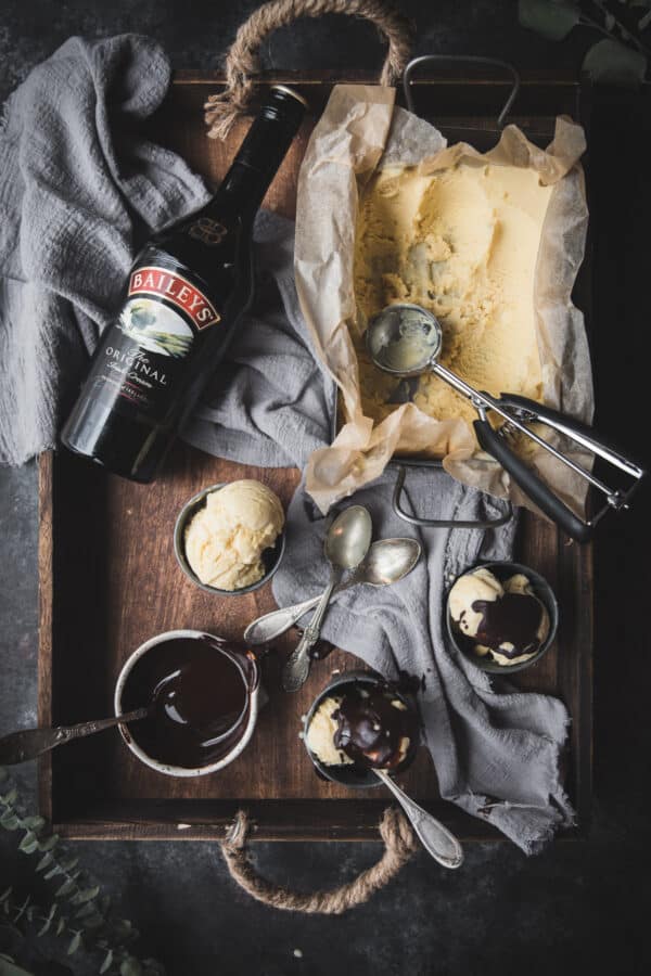 scoops of baileys ice cream in tin cups on a wooden tray with a bottle of baileys