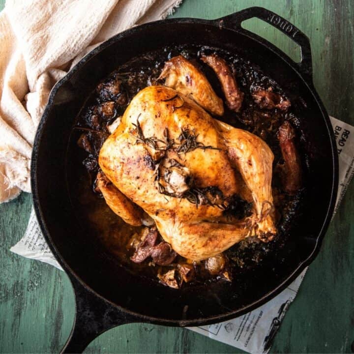 overhead of roasted chicken in a cast iron pan with rosemary and garlic on top