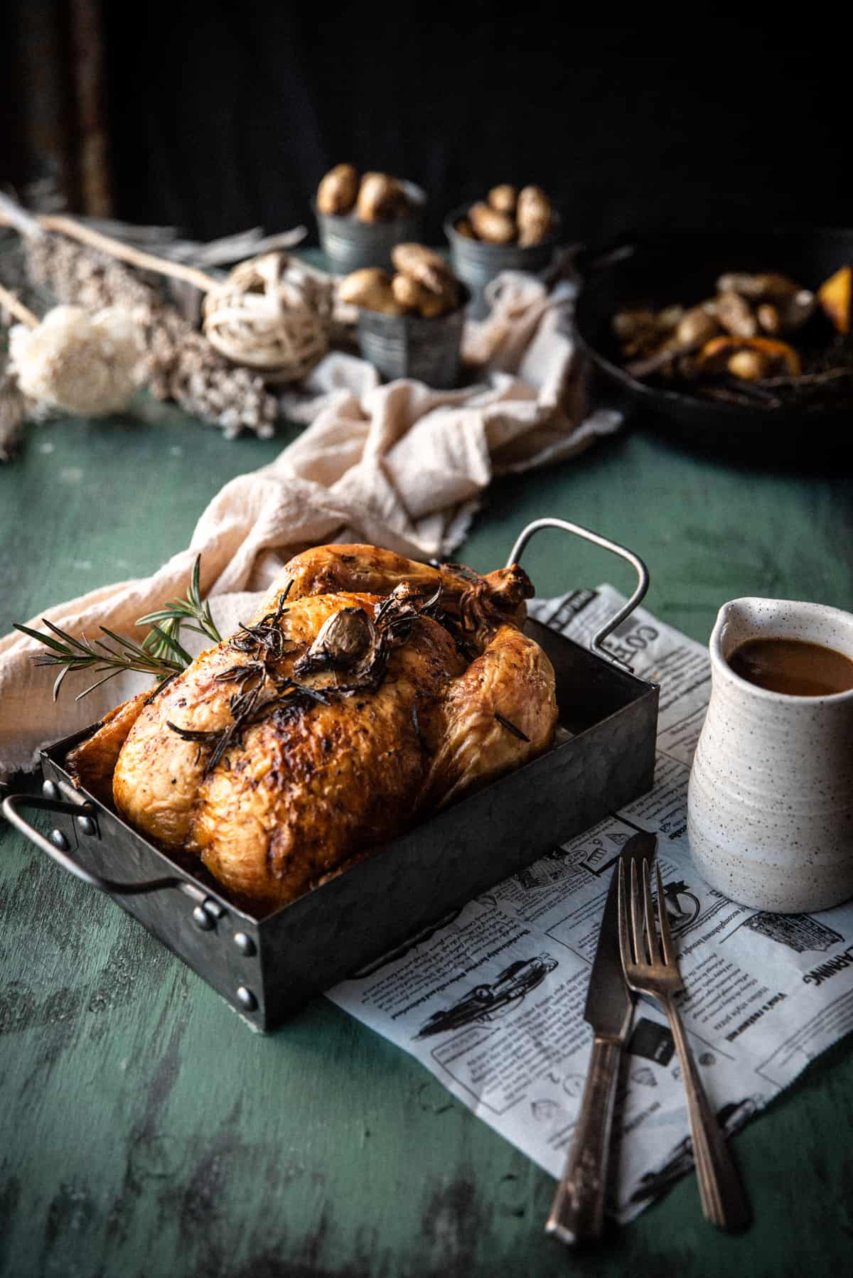 Whole roasted chicken in a stainless steel serving platter with carafe of gravy