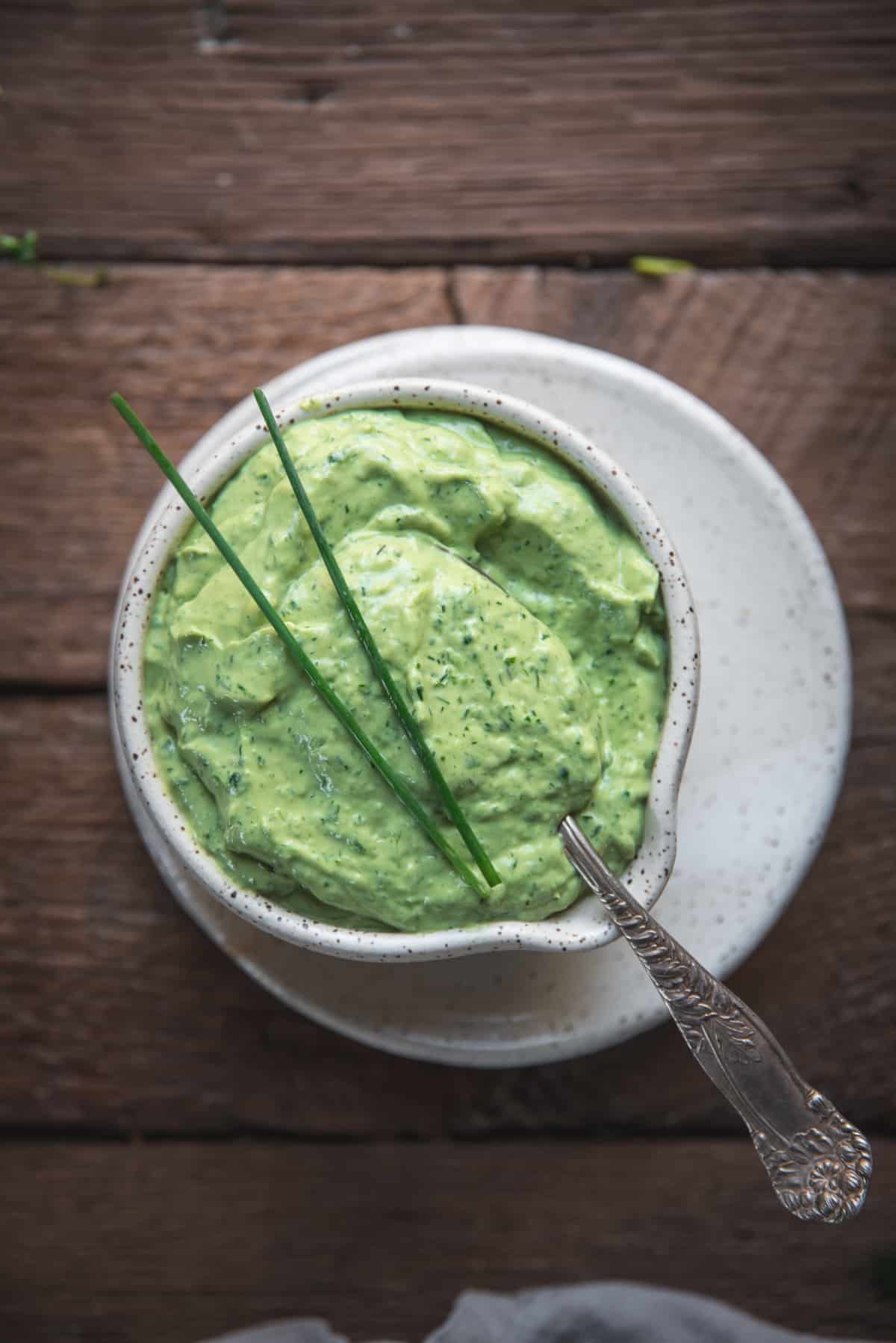 close up of green goddess dressing in a bowl topped with pieces of chive