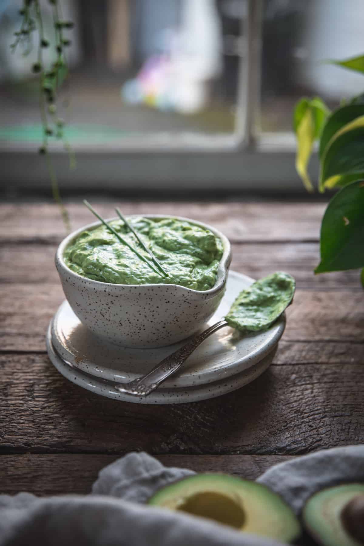 backlit bowl of green dressing with coated spoon on a plate