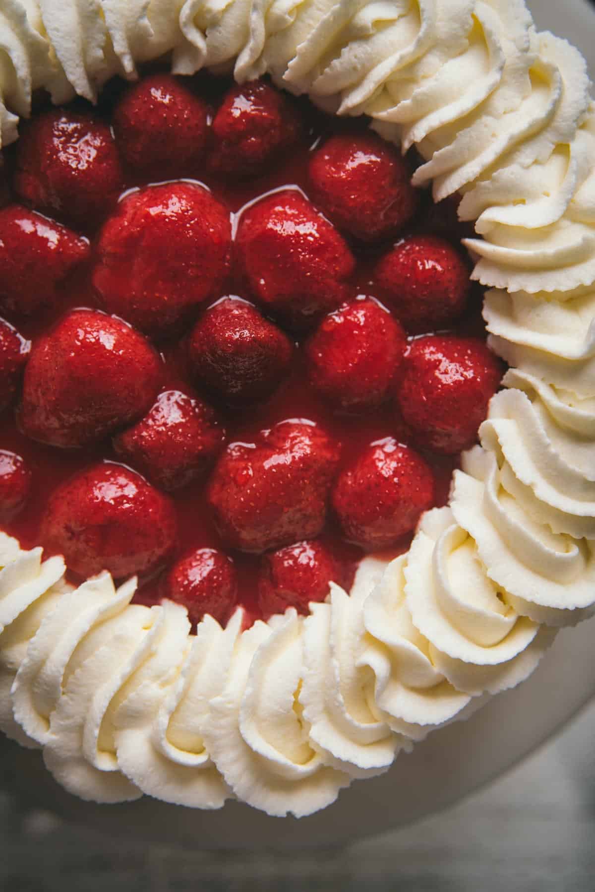 close up of whole strawberry topping surrounded by pipped whipped cream on top of cake