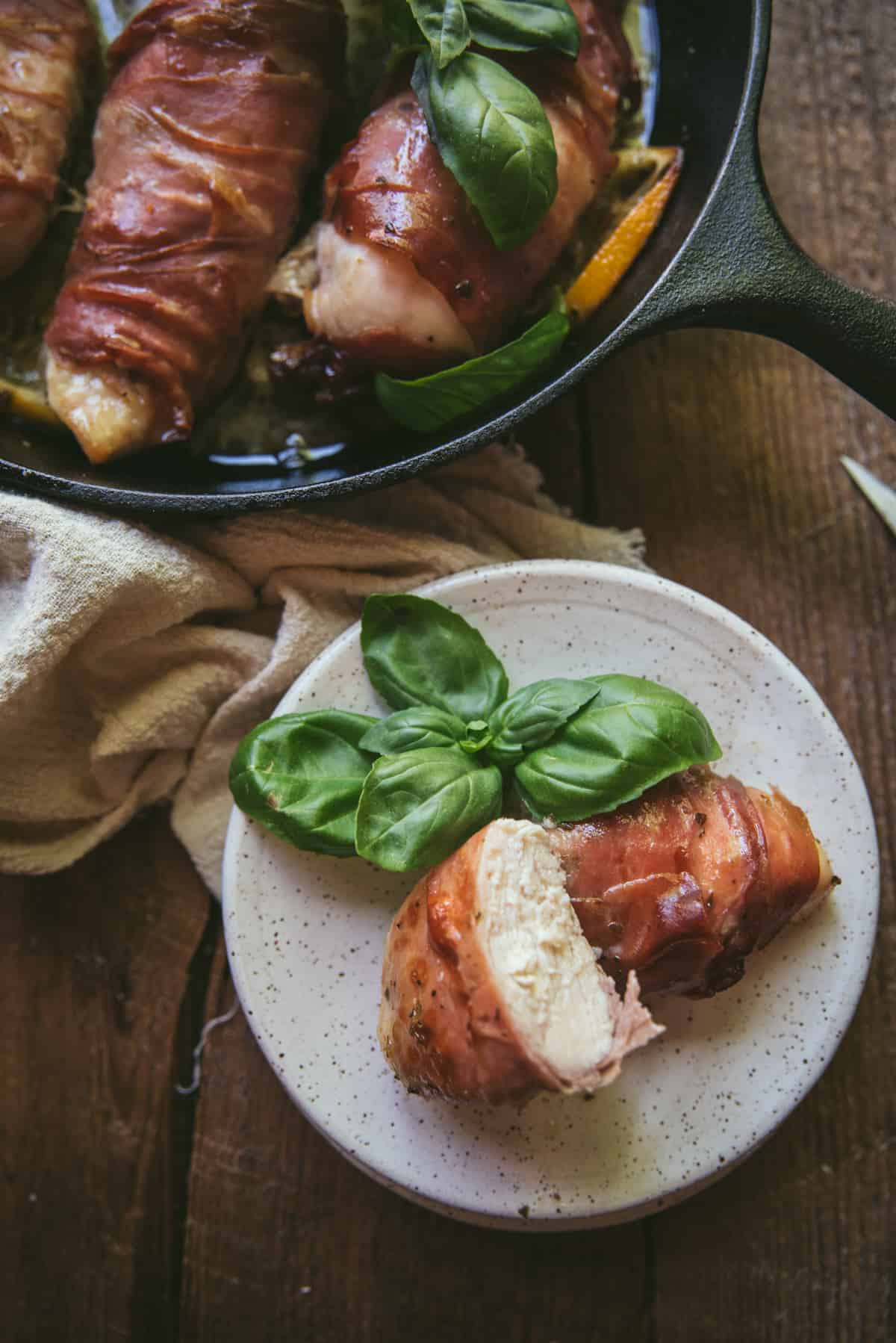 sliced baked chicken on a plate with a skillet full of baked chicken and sauce above it