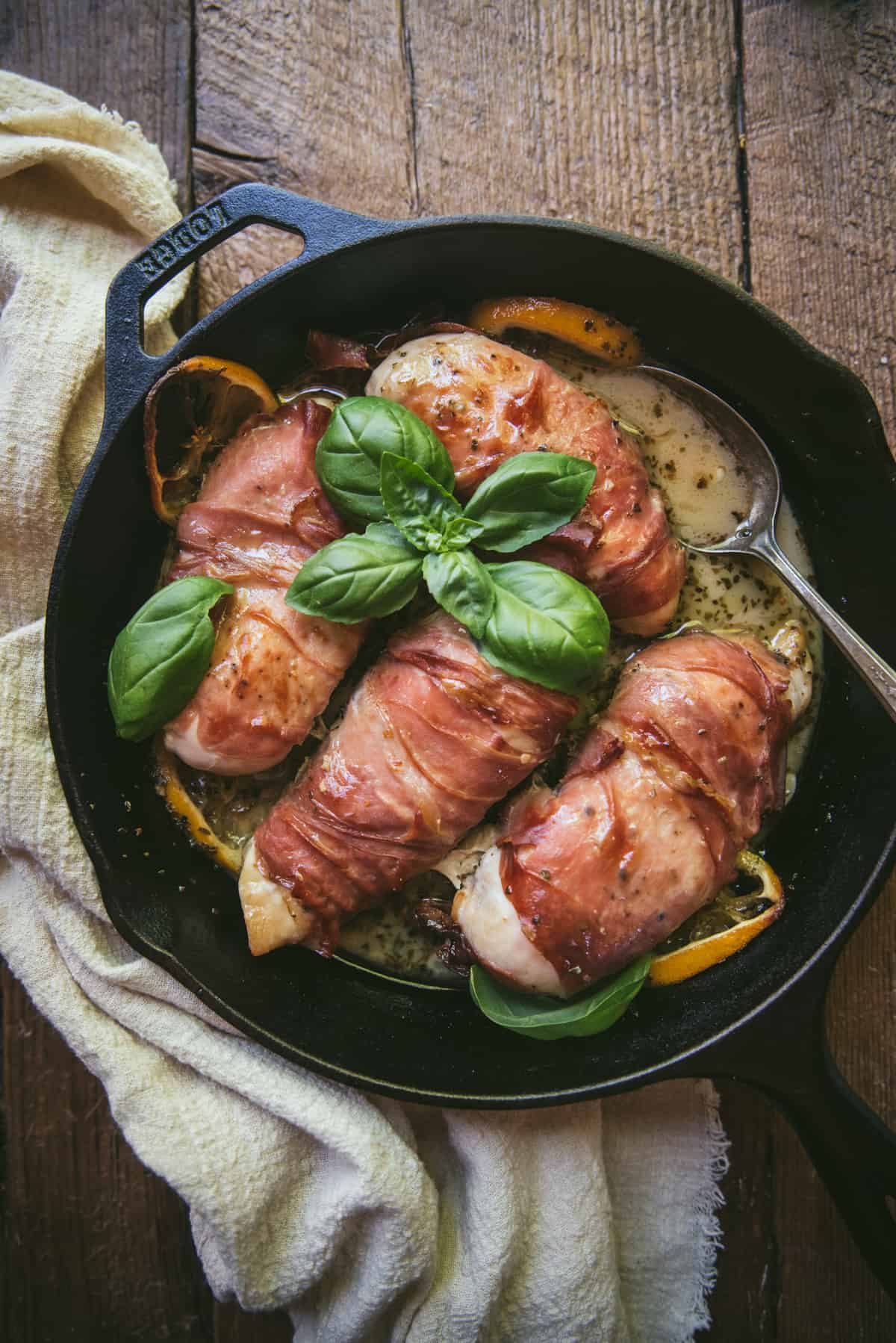 prosciutto wrapped chicken in a cast iron skillet with wine sauce