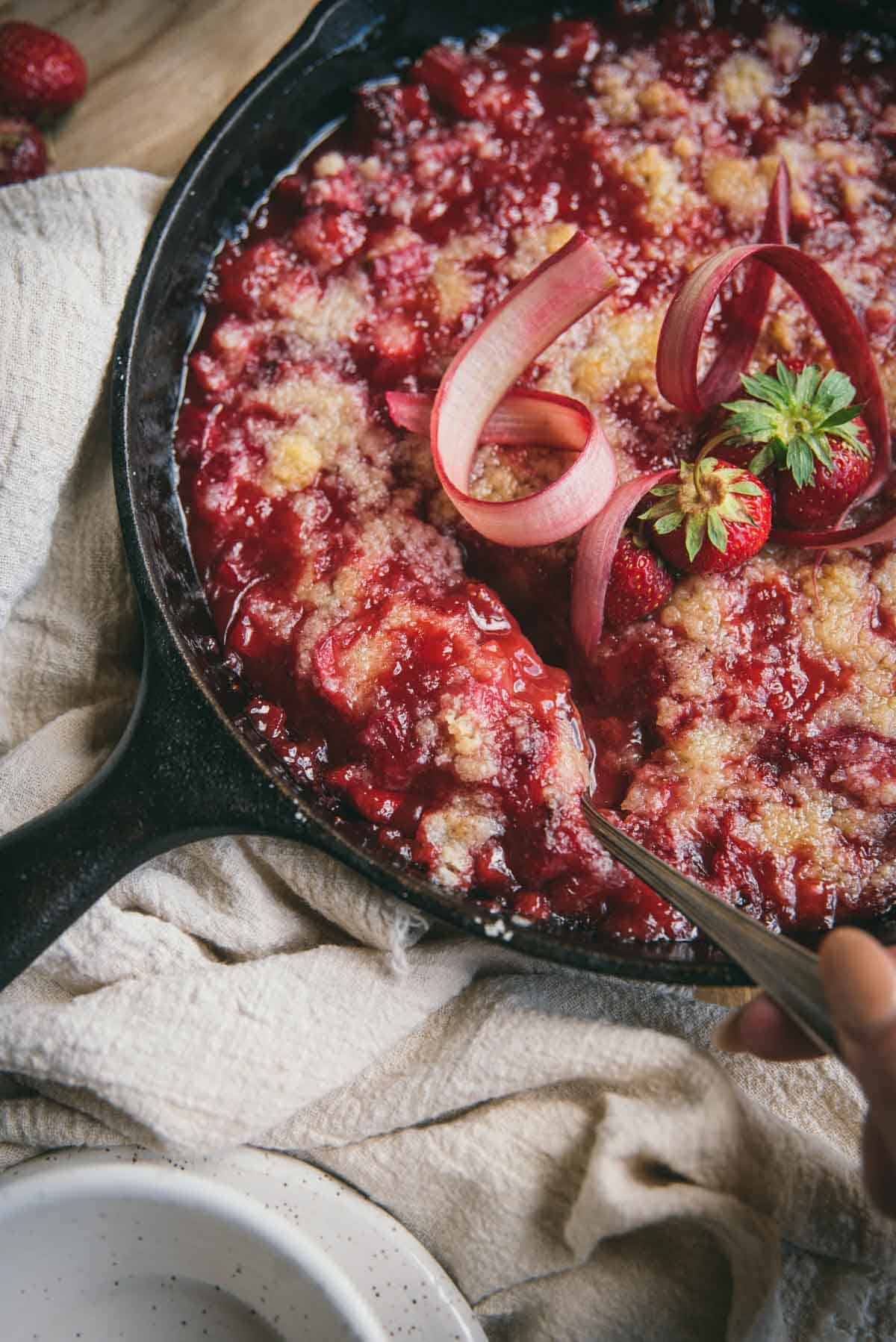 spoon scooping fruit crumble out of a cast iron pan that is on top of a linen napkin