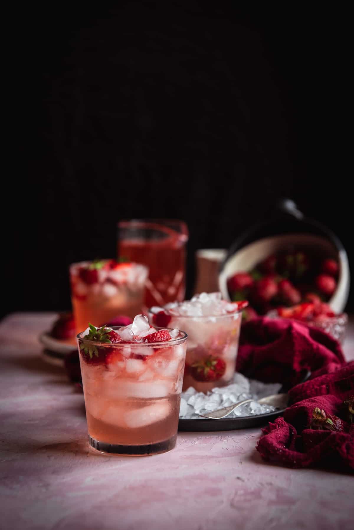 pink sangria in a glass with ice topped with strawberries with more glasses and strawberries in the background