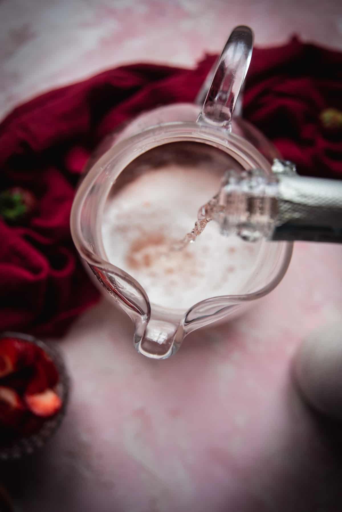 overhead POV of sparking rosé wine pouring into a pitcher