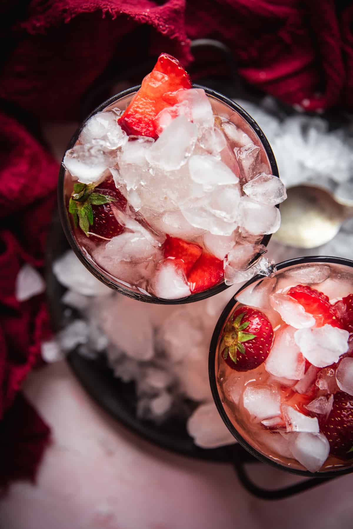 close up overhead of two cocktail glasses with pink cocktails and filled with crushed ice and fresh strawberries