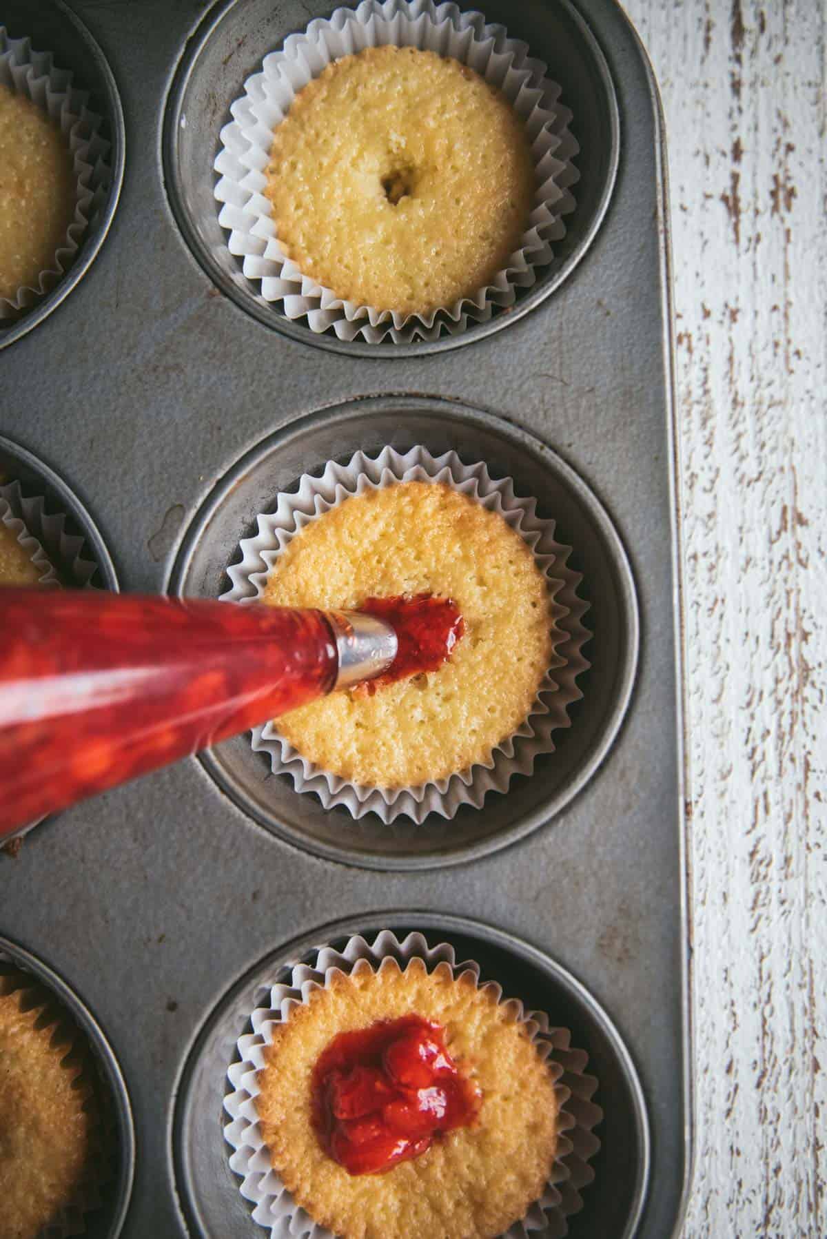 overhead image of cupcakes in a cupcake pan with the cores removed and being filled with strawberry filling