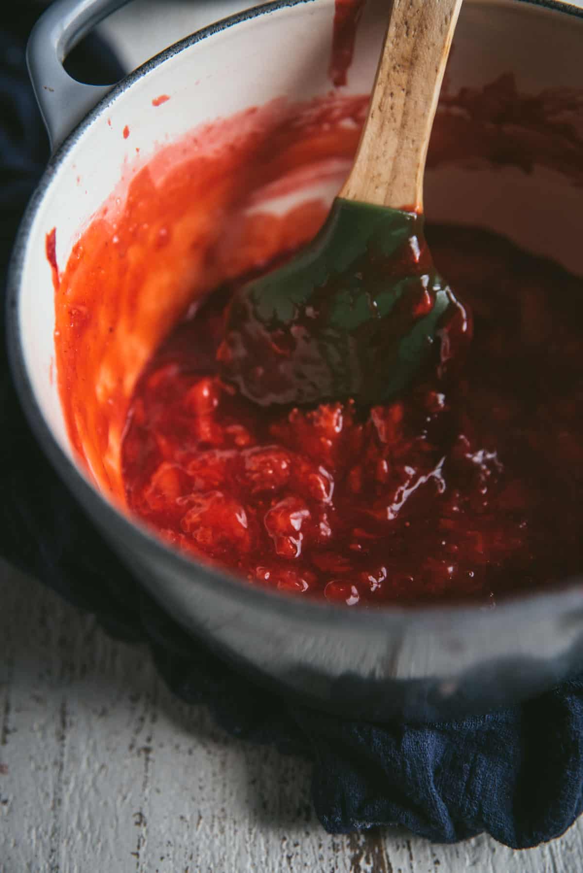 finished strawberry topping being stirred by a green spatula in a saucepan