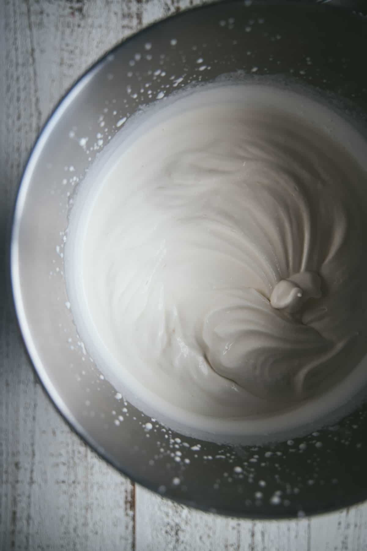 overhead of whipped cream being made in a mixing bowl at the soft peak stage.